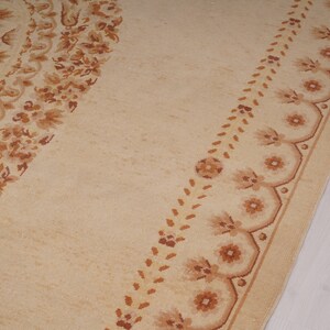 Puede incluir: Una alfombra beige con un patr&oacute;n floral marr&oacute;n. La alfombra tiene un dise&ntilde;o circular en el centro y un borde con un motivo floral repetitivo.