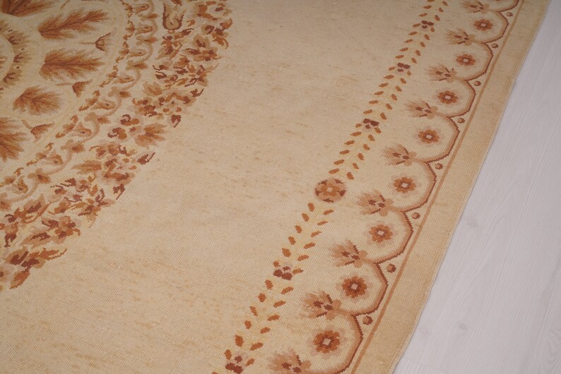 Puede incluir: Una alfombra beige con un patr&oacute;n floral marr&oacute;n. La alfombra tiene un dise&ntilde;o circular en el centro y un borde con un motivo floral repetitivo.