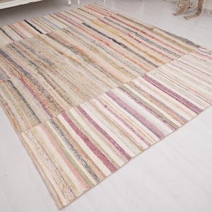 May include: A rectangular area rug featuring a multi-colored striped pattern with various shades of pink, beige, cream, and muted earth tones. The woven textile displays a textured surface with horizontal lines running across the entire length.
