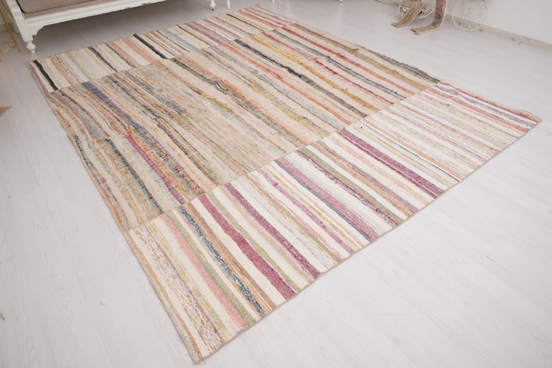 May include: A rectangular area rug featuring a multi-colored striped pattern with various shades of pink, beige, cream, and muted earth tones. The woven textile displays a textured surface with horizontal lines running across the entire length.
