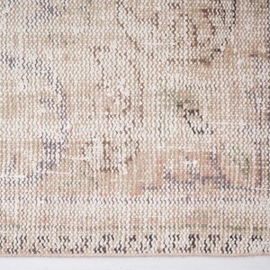 Op de afbeelding: Een close-up van een beige kleed met een subtiel patroon. Het kleed heeft een roze franje langs de rand.