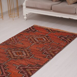 May include: A long, narrow rug with a geometric pattern in shades of orange, brown, and white. The rug has a fringed edge and is made of a soft, woven material.