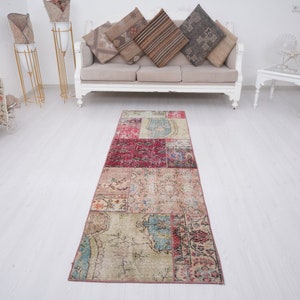 Può includere: Un tappeto lungo e rettangolare in patchwork con una varietà di colori e motivi. Il tappeto è composto da diversi pezzi di tessuto più piccoli che sono stati cuciti insieme. Il tappeto ha un aspetto e una sensazione vintage.