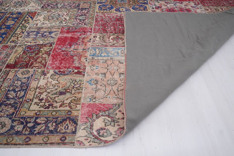K&ouml;nnte beinhalten: Ein Patchwork-Teppich mit verschiedenen Farben und Mustern, darunter Rot, Blau und Beige. Der Teppich hat eine graue R&uuml;ckseite und ist in der Mitte gefaltet.