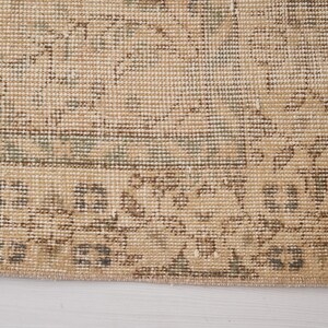 May include: Close-up of a section of a beige and green patterned rug. The rug has a distressed, vintage look with intricate floral and geometric designs. The edges are frayed.