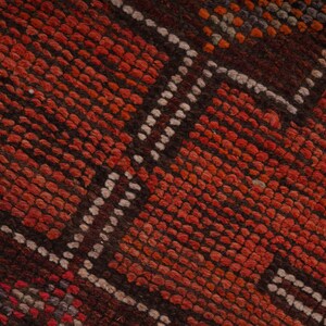 May include: Close-up of a red and brown woven rug with a geometric pattern. The rug has a textured surface and is made of natural fibers.