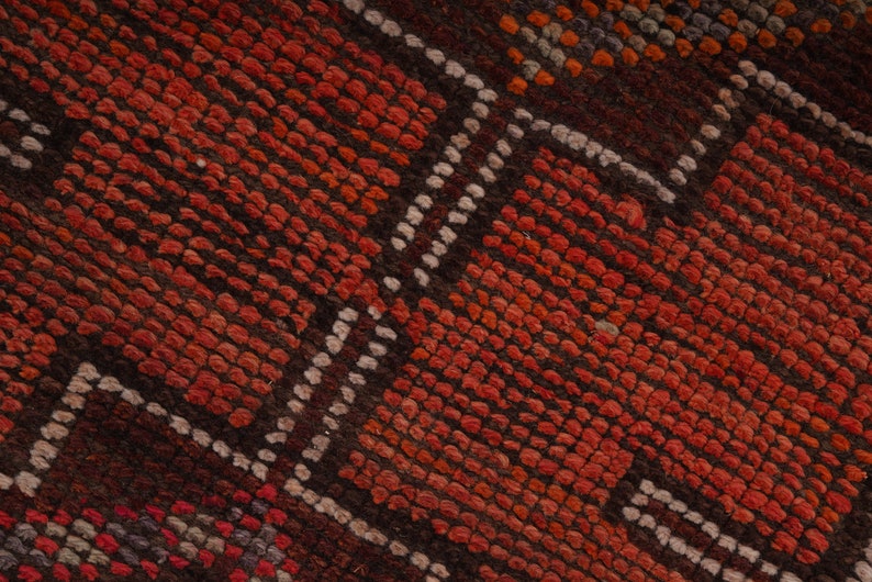 May include: Close-up of a red and brown woven rug with a geometric pattern. The rug has a textured surface and is made of natural fibers.