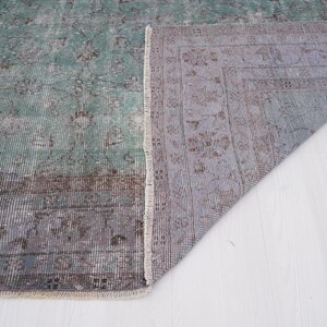 May include: A vintage rug with a faded green and brown pattern. The rug is folded in half, showing the underside, which is a light gray with a subtle pattern.
