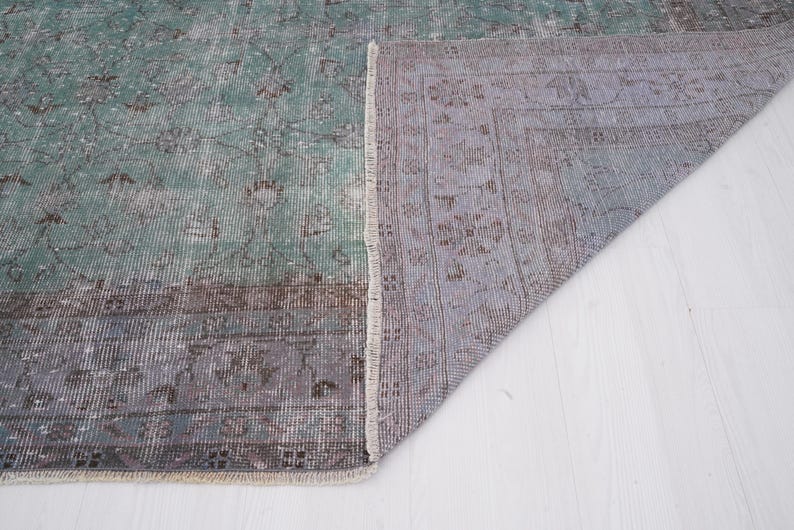 May include: A vintage rug with a faded green and brown pattern. The rug is folded in half, showing the underside, which is a light gray with a subtle pattern.