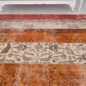 Puede incluir: Una alfombra rectangular con un dise&ntilde;o de patchwork de bandas horizontales. La alfombra muestra secciones alternas de naranja vibrante, crema y rojo intenso, decoradas con intrincados patrones florales, enredaderas y motivos bot&aacute;nicos detallados.