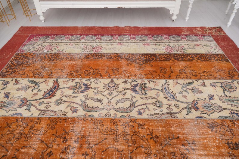 Puede incluir: Una alfombra rectangular con un dise&ntilde;o de patchwork de bandas horizontales. La alfombra muestra secciones alternas de naranja vibrante, crema y rojo intenso, decoradas con intrincados patrones florales, enredaderas y motivos bot&aacute;nicos detallados.