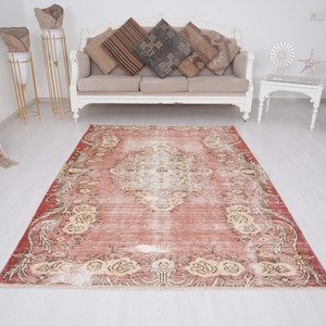 May include: A rectangular area rug featuring a faded terracotta red base with a central cream-coloured medallion and intricate floral border patterns in shades of beige and white, displaying a distressed texture throughout the surface.
