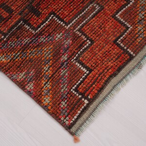 May include: Close-up of the edge of a red, orange, and brown patterned rug with a fringe. The rug has a geometric design.