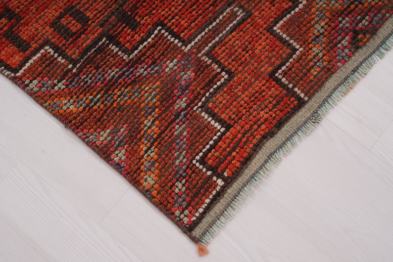 May include: Close-up of the edge of a red, orange, and brown patterned rug with a fringe. The rug has a geometric design.