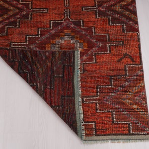 May include: A red, brown, and blue patterned rug with a geometric design. The rug is folded in half and the underside is visible.