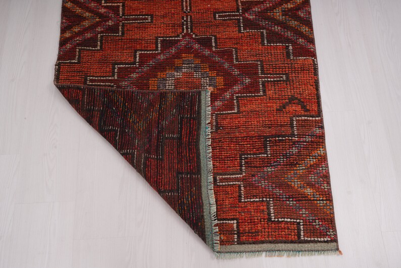May include: A red, brown, and blue patterned rug with a geometric design. The rug is folded in half and the underside is visible.