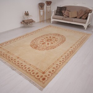Puede incluir: Una alfombra beige con un gran dise&ntilde;o ovalado intrincado en un tono marr&oacute;n m&aacute;s oscuro. La alfombra tiene un borde con flecos.