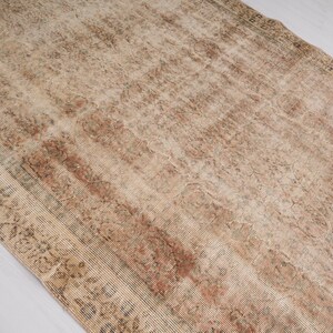 May include: A rectangular, distressed rug with a faded, vintage appearance. The rug features a blend of beige, brown, and reddish-brown hues, with intricate floral and geometric patterns. The rug's design suggests it is an antique or a rug with a vintage aesthetic.