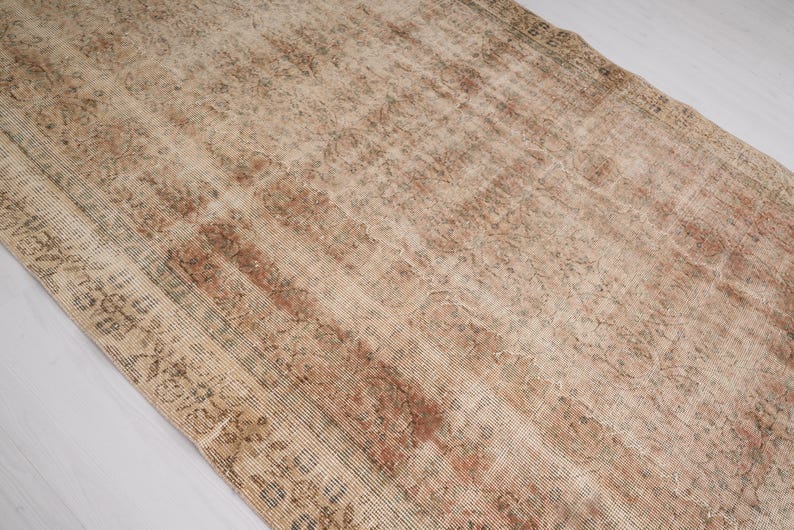 May include: A rectangular, distressed rug with a faded, vintage appearance. The rug features a blend of beige, brown, and reddish-brown hues, with intricate floral and geometric patterns. The rug's design suggests it is an antique or a rug with a vintage aesthetic.