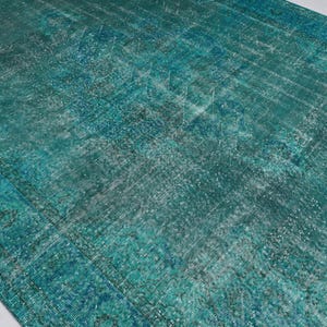 May include: A vintage teal blue rug with a faded, distressed pattern. The rug has a worn, antique look and is made of a soft, textured material.