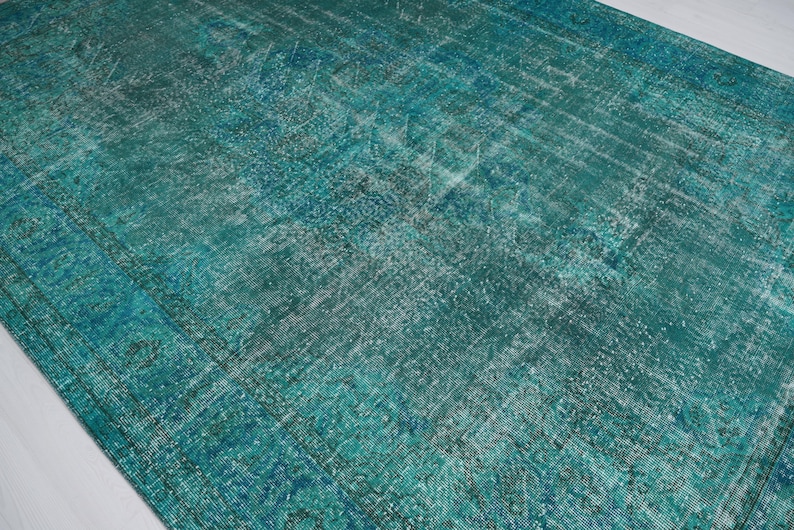 May include: A vintage teal blue rug with a faded, distressed pattern. The rug has a worn, antique look and is made of a soft, textured material.