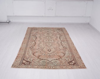 May include: A vintage rug with a beige background and a brown and green floral pattern. The rug has a worn and faded look, giving it a rustic charm.