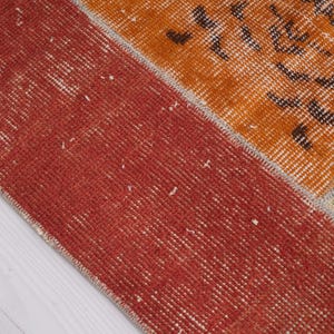 Puede incluir: Una alfombra rectangular con dise&ntilde;o de patchwork que presenta un borde ancho de color rojo s&oacute;lido en el lado izquierdo. Las secciones restantes muestran paneles de color naranja vibrante y crema adornados con intrincados patrones florales y geom&eacute;tricos.