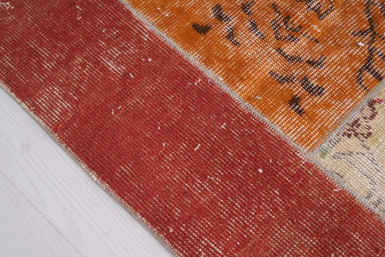 Puede incluir: Una alfombra rectangular con dise&ntilde;o de patchwork que presenta un borde ancho de color rojo s&oacute;lido en el lado izquierdo. Las secciones restantes muestran paneles de color naranja vibrante y crema adornados con intrincados patrones florales y geom&eacute;tricos.