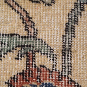 Puede incluir: Una vista de cerca de un tejido con un fondo de color tostado claro y un patr&oacute;n floral detallado. El dise&ntilde;o incluye hojas estilizadas en verde apagado, contornos oscuros y acentos en rojo intenso y azul tejidos en la textura de la tela.