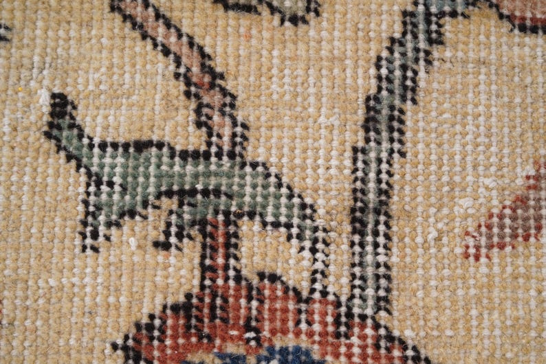 Puede incluir: Una vista de cerca de un tejido con un fondo de color tostado claro y un patr&oacute;n floral detallado. El dise&ntilde;o incluye hojas estilizadas en verde apagado, contornos oscuros y acentos en rojo intenso y azul tejidos en la textura de la tela.