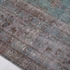 May include: Close-up of a vintage rug with a faded blue and brown pattern. The rug has a distressed look and a woven texture.