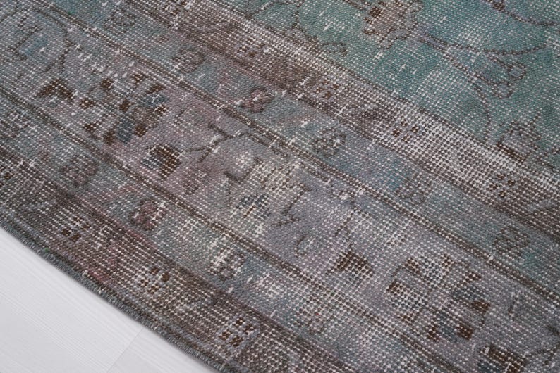 May include: Close-up of a vintage rug with a faded blue and brown pattern. The rug has a distressed look and a woven texture.