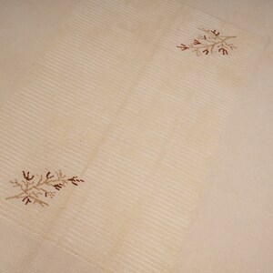 Pu&ograve; includere: Un tappeto beige con una texture leggermente rigata e due disegni floreali ricamati marroni.