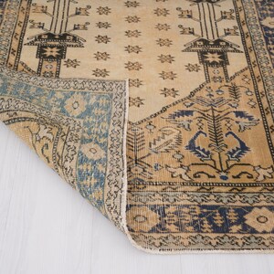 May include: A vintage rug with a beige background and blue and brown geometric patterns. The rug has a fringed edge and is folded in half.