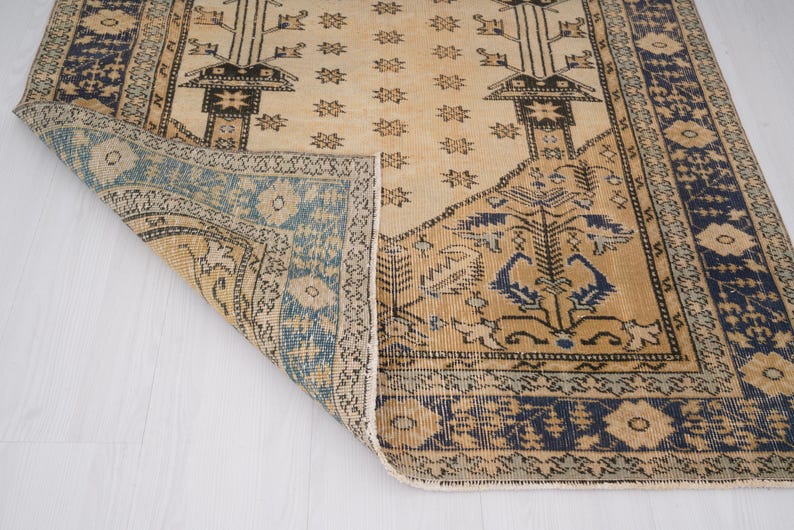 May include: A vintage rug with a beige background and blue and brown geometric patterns. The rug has a fringed edge and is folded in half.