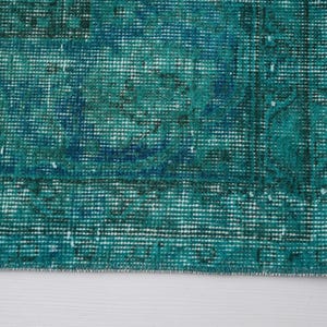 May include: Close-up of a teal blue rug with a woven texture and frayed edges.