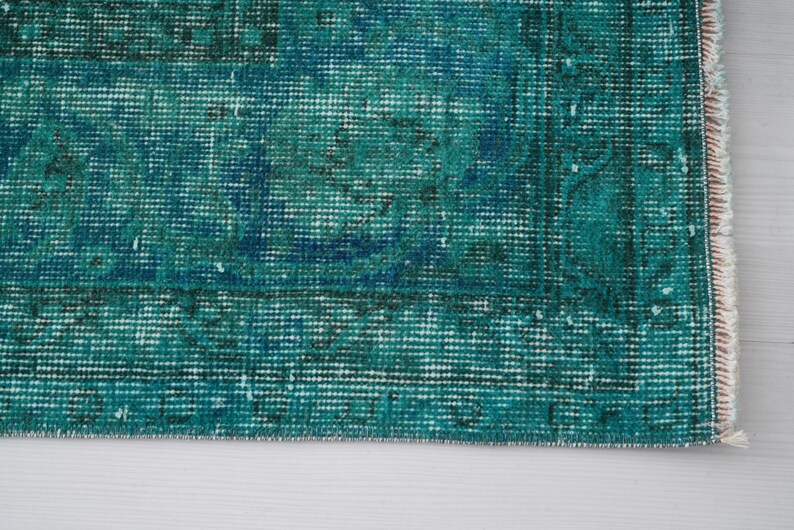 May include: Close-up of a teal blue rug with a woven texture and frayed edges.