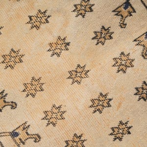 May include: A close-up of a beige rug with a repeating pattern of black stars and geometric shapes.
