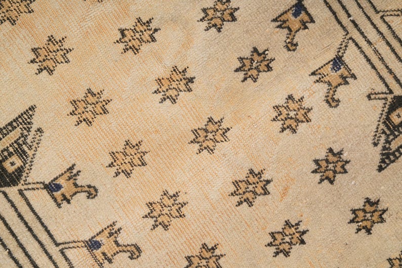 May include: A close-up of a beige rug with a repeating pattern of black stars and geometric shapes.