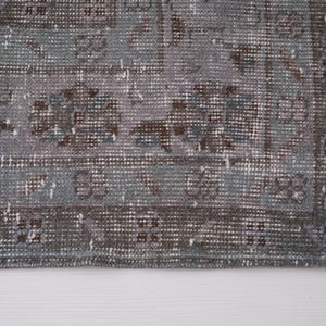 May include: A vintage rug with a faded blue and brown pattern. The rug has a fringed edge and is made of a soft, woven material.