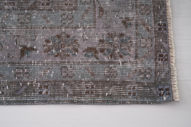 May include: A vintage rug with a faded blue and brown pattern. The rug has a fringed edge and is made of a soft, woven material.