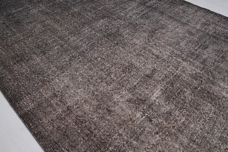 May include: A close-up of a dark gray rug with a subtle pattern. The rug has a distressed, vintage look and is made of a soft, woven material.