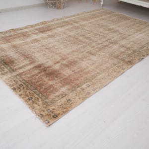 May include: A rectangular, distressed-look rug with a faded, vintage appearance. The rug features a central field of beige and brown tones, with a darker border. The design includes floral and geometric patterns.