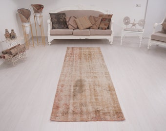 May include: A long, rectangular, vintage-style rug in shades of beige, brown, and pink. The rug has a distressed, faded look and is laid out on a white floor.