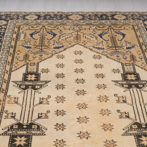 May include: A beige prayer rug with a blue and beige border. The rug has a traditional design with a central motif of a stylized tree and stars.