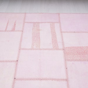 May include: A pink patchwork rug with a variety of textures and patterns. The rug is made of different pieces of fabric sewn together.