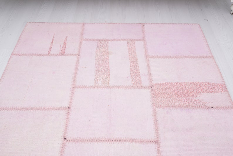 May include: A pink patchwork rug with a variety of textures and patterns. The rug is made of different pieces of fabric sewn together.