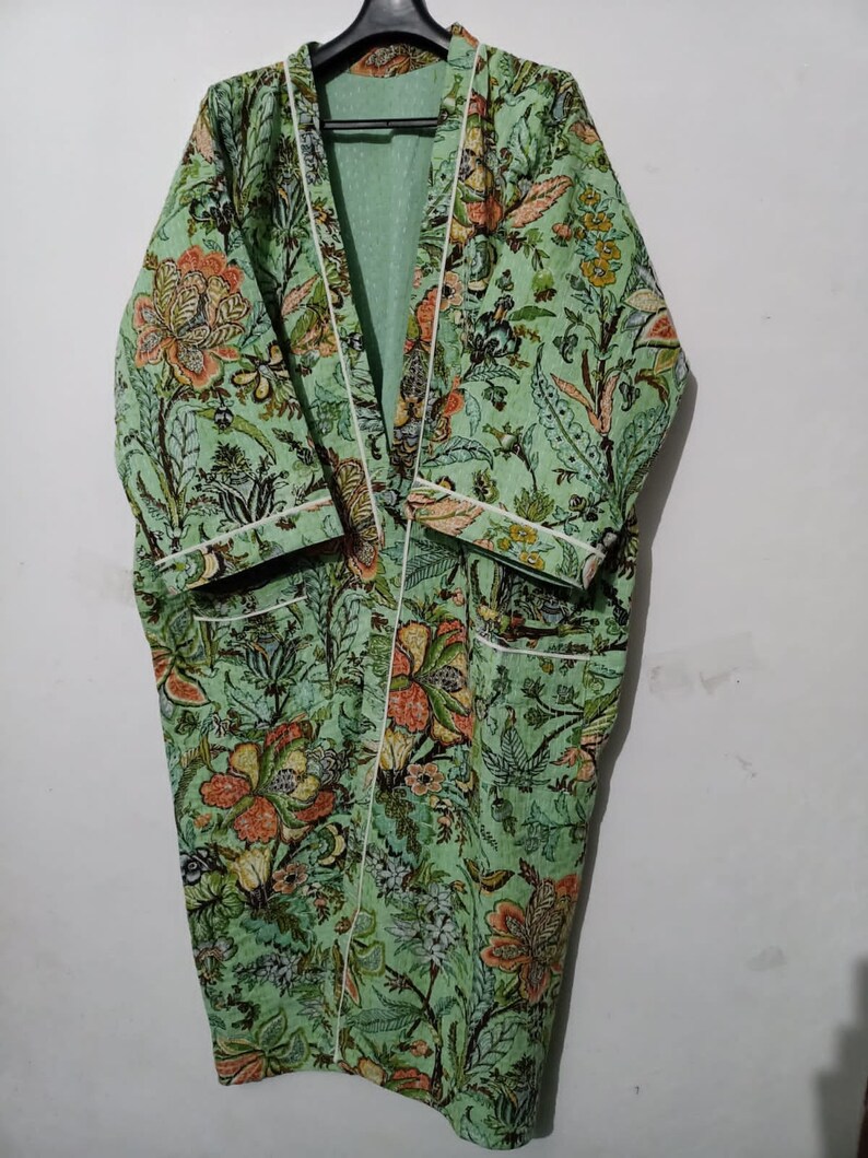May include: A green floral print robe with white piping. The robe has a long, flowing silhouette and a shawl collar.