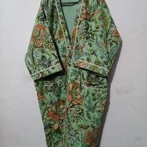 May include: A green floral print robe with white piping around the edges. The robe has a long, flowing silhouette and a shawl collar.