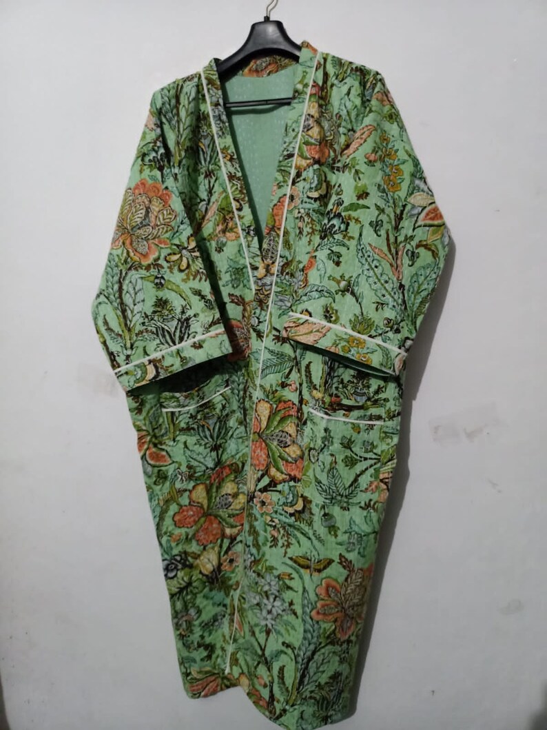 May include: A green floral print robe with white piping around the edges. The robe has a long, flowing silhouette and a shawl collar.